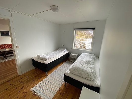 Gemütliches Schlafzimmer in Nord-Norwegen mit zwei Einzelbetten, Holzboden und Fensterblick auf die beeindruckende Küstenlandschaft. Ideal für entspannenden Angelurlaub in skandinavischer Naturkulisse.