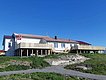 Traditionelles, weißes Gebäude in Nordland, Norwegen, mit rotem Dach und norwegischer Flagge. Umgeben von grünen Wiesen und malerischem blauen Himmel. Ideal für Angelurlaub und Naturerlebnisse in einer beeindruckenden, ruhigen Umgebung.