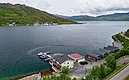 Küste Nord-Norwegens: Malerische Fjorde und grüne Hügel umrahmen traditionelle Holzhütten und Boote. Beliebtes Ziel für Angelreisen und Naturabenteuer mit atemberaubender Landschaft und idealen Bedingungen für Angelurlauber.