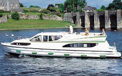 Ein großes, weißes Motorboot fährt auf einem Fluss, während im Hintergrund eine Steinbrücke und grüne Landschaft zu sehen sind.