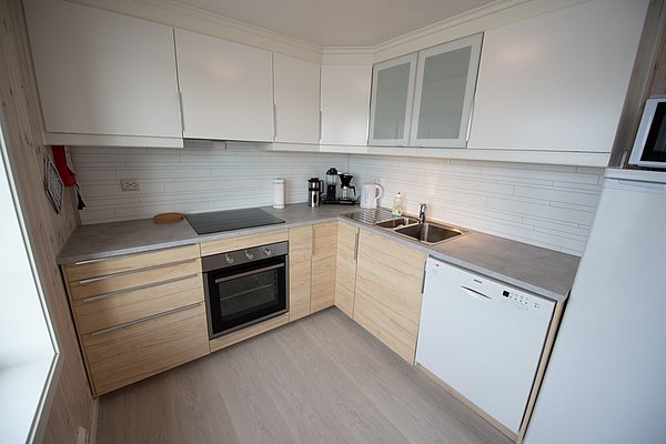 Moderne Küche mit weißen und holzfarbenen Schränken, ausgestattet mit einem Herd, Ofen, Spüle, Geschirrspüler und Kaffeemaschine.