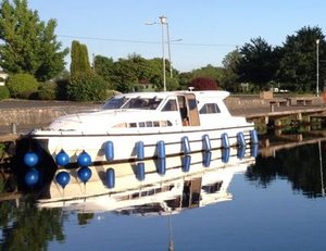 Ein weißes Hausboot mit blauen Fendern liegt ruhig vertäut am River Shannon in Irland. Die klare Spiegelung im Wasser und die grüne Umgebung schaffen eine idyllische und entspannende Atmosphäre für Natur- und Angelurlaub.