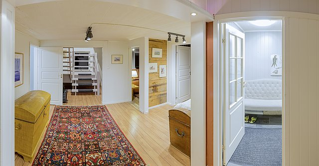 Helles, gemütliches Interieur in Nordland, Norwegen: Holzböden, bunter Teppich, Treppe, Möbel aus Holz, weiße Wände. Charmante, skandinavische Einrichtung für einen erholsamen Angelurlaub. Ideal für Naturliebhaber und Abenteuerlustige.