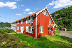 Rotes Holzhaus in Süd-Norwegen, umgeben von grüner Landschaft und Bergen, ideal für Angelreisen. Traditionelle Architektur, malerische Umgebung, perfekte Basis für Abenteuer. Entspanne in der Natur dieser idyllischen skandinavischen Region.