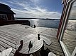 Sonnige Terrasse mit Blick auf das glitzernde Meer in Hitra, Norwegen. Gemütliche Holzbank und Tisch laden zur Entspannung ein – perfekt für einen erholsamen Angelurlaub. Malerische Aussicht und frische Seeluft.