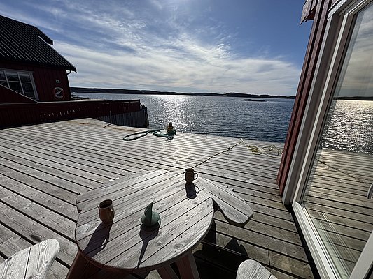 Sonnige Terrasse mit Blick auf das glitzernde Meer in Hitra, Norwegen. Gemütliche Holzbank und Tisch laden zur Entspannung ein – perfekt für einen erholsamen Angelurlaub. Malerische Aussicht und frische Seeluft.