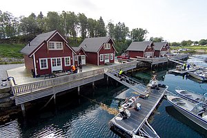 Gemütliche rote Rorbuer (Fischerhütten) direkt am Wasser in Nordland, Norwegen mit Anlegestegen und Booten – ideales Angelurlaubsziel für Naturliebhaber und Abenteurer. Perfekte Basis für Meeresangeln und Erkundungen in malerischer Umgebung.