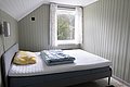 Gemütliches Schlafzimmer in Hitra, Norwegen mit hellem Holzwand-Design, großem Fenster und gemütlichem Bett. Ideal für Angelreisende auf der Suche nach Entspannung und Naturverbundenheit. Perfekter Rückzugsort nach einem fischreichen Angeltag.