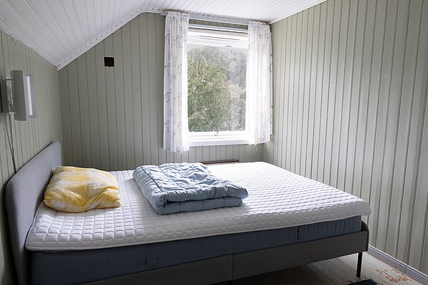 Gemütliches Schlafzimmer in Hitra, Norwegen mit hellem Holzwand-Design, großem Fenster und gemütlichem Bett. Ideal für Angelreisende auf der Suche nach Entspannung und Naturverbundenheit. Perfekter Rückzugsort nach einem fischreichen Angeltag.
