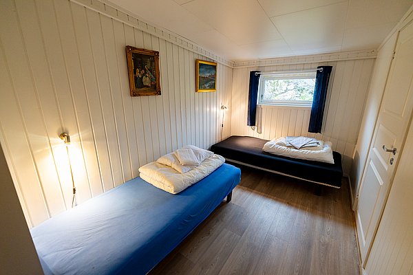 Gemütliches Schlafzimmer in Nordland, Norwegen mit zwei Einzelbetten, hellen Holzwänden, stilvoller Beleuchtung und Naturblick. Ideal für erholsame Nächte während eines Angelurlaubs. Perfekte Kombination aus Komfort und rustikalem Charme.