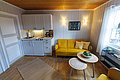Gemütliches Ferienhaus in Hitra, Norwegen: heller Raum mit gelbem Sofa, rustikaler Holzwand, kleiner Küchenzeile und skandinavischem Dekor. Ideal für Angelurlaub und Erholung in malerischer Umgebung. Perfekte Ausgangsbasis für Abenteuer in der Natur.