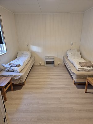 Ein einfaches, gemütliches Schlafzimmer in Nord-Norwegen mit zwei Einzelbetten, hellem Holzfußboden und natürlichem Licht – ideal für entspannende Angelurlaube.