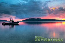 Ein Boot schwimmt auf einem stillen Fjord in Südwest-Norwegen. Dramatischer Sonnenuntergang färbt den Himmel in Rosa und Blau. Perfekter Angelurlaub in atemberaubender Naturkulisse.