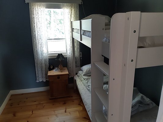 Ein schlicht eingerichtetes Schlafzimmer mit einem Etagenbett, blau gestrichenen Wänden und einem Fenster mit weißen Spitzenvorhängen.