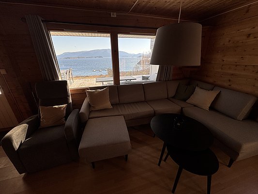 Gemütliches Wohnzimmer in einer norwegischen Hütte auf Hitra, mit großer Fensterfront und Blick aufs Meer. Perfekt für Angelurlaub in Norwegen, Entspannung und Naturgenuss. Ruhige Atmosphäre mit skandinavischem Design.