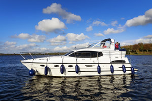 Ein elegantes Hausboot gleitet auf dem River Erne in Irland, eingefasst von blauem Himmel und weißen Wolken, ideale Bedingungen für Angelreisen. Perfekte Mischung aus Natur, Komfort und Abenteuer auf dem Wasser.