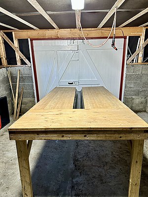 Rustikaler Holzarbeitstisch in einer Holzhütte in Nord-Norwegen. Unbearbeitete Wände und schlichte Beleuchtung schaffen eine einfache, funktionelle Atmosphäre, ideal für handwerkliche Arbeiten.