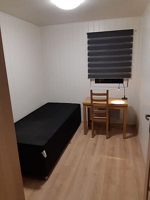 Kompaktes, gemütliches Zimmer in Nordland, Norwegen, mit Einzelbett, kleinem Schreibtisch und Lampe. Perfekt für Erholung nach einem erlebnisreichen Angeltag in beeindruckender Naturkulisse. Ideale Unterkunft für Angelbegeisterte.