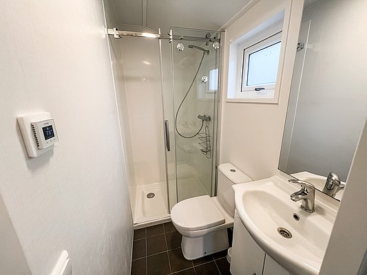 Kompaktes, modernes Badezimmer in Nord-Norwegen mit bodenebener Dusche, weißem Waschbecken und WC. Minimalistisches Design mit Tageslichtfenster. Ideal für komfortable Angelreisen.
