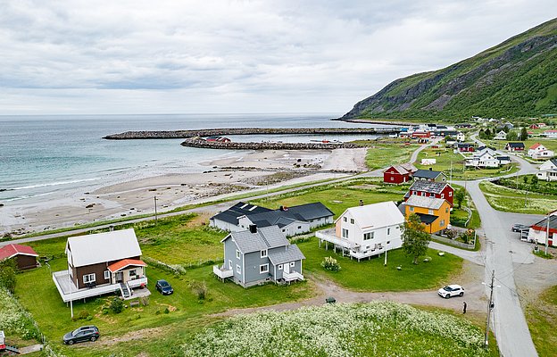 Küstenort in Nord-Norwegen mit bunten Häusern, grünen Wiesen und schroffer Küstenlinie. Idealer Ausgangspunkt für Angelreisen, umgeben von beeindruckender Naturkulisse und dem ruhigen Meer. Perfekte Bedingungen für Abenteurer und Naturliebhaber.