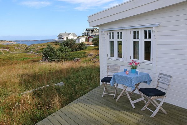 Eine gemütliche Terrasse mit Tisch und Stühlen auf einem Holzdeck, umgeben von grüner Landschaft und küstennaher Aussicht in der Region Hitra, Norwegen, ideal für Angelreisen und Naturliebhaber.