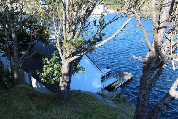 Weiße Bootshütte am Wasser, umgeben von Bäumen, in Südwest-Norwegen. Perfekt für Angelreisen und Meeresangeln. Beruhigende Naturkulisse und idealer Ausgangspunkt für unvergessliche Abenteuer.