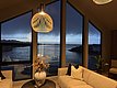 Gemütlicher Wohnbereich mit modernen Lampen, Blick auf dramatische Küstenlandschaft von Südwest-Norwegen. Große Fenster zeigen das Meer bei Dämmerung, stilvolle Einrichtung und Pflanzen schaffen entspannte Atmosphäre. Ideal für Angelurlaub und Naturerlebnis.