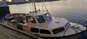 Ein kleines, weißes Fischerboot mit der Aufschrift "VÅGSBUEN" liegt an einem Holzsteg in einem ruhigen Hafen bei Sonnenuntergang. Ein kleines, weißes Fischerboot mit der Aufschrift "VÅGSBUEN" liegt an einem Holzsteg in einem ruhigen Hafen bei Sonnenuntergang.