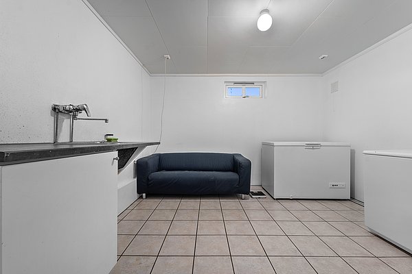 Eine schlichte weiße Waschküche in Nord-Norwegen mit Fliesenboden, blauer Couch, zwei großen Gefriertruhen und einem Waschbecken – perfekt für Angelurlaube zur Fischverarbeitung und Lagerung.