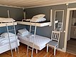 Ein modernes Zimmer mit Etagenbetten, hellgrauen Wänden, einer Holzdecke und einem Holzfußboden, ausgestattet mit Leiter, Spiegel und Stuhl.