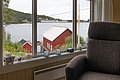 Blick aus einem gemütlichen Zimmer auf ein rotes Bootshaus am Wasser in Norwegen. Malerische Landschaft der Region Hitra, ideal für einen erholsamen Angelurlaub. Naturnahe Entspannung am malerischen Fjord.