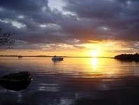 Ein Sonnenuntergang über einem ruhigen See, auf dem ein Boot schwimmt, unter einem teils bewölkten Himmel.