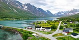 Luftaufnahme einer idyllischen Fjordlandschaft in Nord-Norwegen: klare Gewässer, malerische Hütten, majestätische Berge mit Schnee. Perfektes Reiseziel für Angelurlaub und Naturerlebnisse in atemberaubender skandinavischer Kulisse.