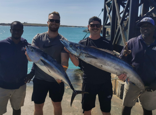 Vier Angler posieren stolz mit ihren großen Fängen in Boa Vista, Kapverden, vor einem malerischen, tiefblauen Meerespanorama – ideal für Angelreisen und Meeresangeln.
