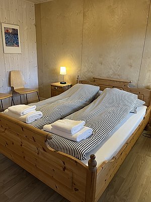 Gemütliches Schlafzimmer mit Holzmöbeln auf Hitra, Norwegen. Doppelbett mit gestreifter Bettwäsche, weichen Handtüchern und Nachttischlampe. Ideal für erholsamen Angelurlaub. Maritime Gemütlichkeit in skandinavischem Design.