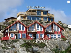 Rote Holzhäuser der Villa Hellesøy in Südwest-Norwegen auf felsigem Hang, mit großen Fenstern und Balkonen, ideal für naturnahe Angelreisen mit Meerblick und komfortabler Unterkunft.