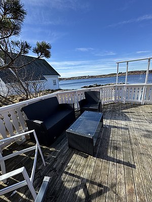 Holzterrasse mit modernen Outdoor-Möbeln und Meerblick in Hitra, Norwegen. Blauer Himmel, malerische Küstenlinie und entspannte Atmosphäre laden zum Verweilen ein. Ideal für Angelurlaub und Naturgenuss.
