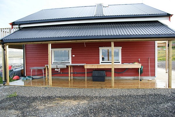 Rotes Holzhaus mit überdachter Terrasse und Fischvorbereitungsstation in Nord-Norwegen. Perfekt für Angelurlaube, bietet es praktischen Komfort und eine ideale Basis für Meeresangeln-Abenteuer.