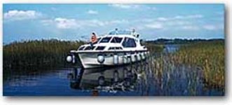 Ein weißes Motorboot fährt durch ein schilfbewachsenes Gewässer unter einem blauen Himmel.