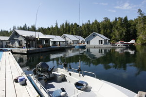 Ruhiger Angelort in Rivers Inlet, Kanada: Boote im Vordergrund, schwimmende Hütten und Wasserflugzeug vor bewaldeter Küste. Perfektes Ziel für Abenteuer- und Meeresangeln.