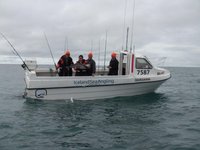 Eine Gruppe von Menschen mit orangefarbenen Mützen steht an Bord eines Angelboots namens "Ödinshani" auf dem Meer, wobei eine Person stolz einen gefangenen Fisch präsentiert.