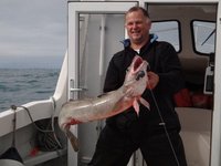 Eine Person hält einen großen, gefangenen Fisch auf einem Boot auf dem offenen Meer.