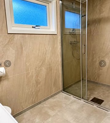 Modernes Badezimmer in Hitra, Norwegen, mit begehbarer Dusche, eleganten beigen Fliesen und Fenster für Tageslicht. Komfortable Unterkunft für Angelreisende. Perfekte Kombination aus Funktionalität und Stil für einen erholsamen Urlaub.
