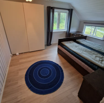 Gemütliches Schlafzimmer in Nordland, Norwegen: Doppelbett, Holzfußboden, minimalistisches Design, blauem Teppich, großem Fenster mit Blick ins Grüne. Ideal für erholsamen Angelurlaub.
