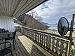 Überdachte Terrasse mit Holzboden, Blick auf norwegische Fjordlandschaft. Sitzmöglichkeiten und Satellitenschüssel links im Bild, ruhige Natur mit Bergen, Meer und Wolken im Hintergrund. Ideal für Angelurlaub in Hitra, Norwegen.