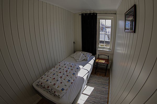 Kleines, gemütliches Einzelzimmer in Nord-Norwegen, mit holzverkleideten Wänden und einem Fenster, das Tageslicht hineinlässt. Ideal für einen erholsamen Angelurlaub.