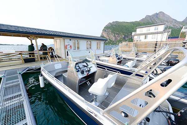 Moderne Angelboote in Nordland, Norwegen, bereit für spannende Angelabenteuer. Malerische Küstenszenerie mit grünen Bergen, Fischerhütte und Steg. Perfekt für Meeresangeln und Naturgenuss.