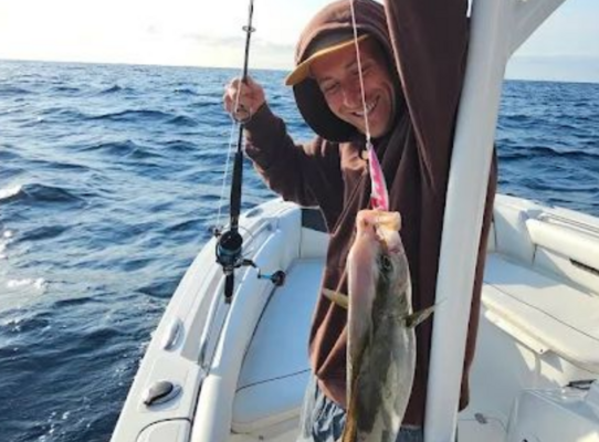 Ein begeisterter Angler hält seinen Fang auf einem Boot vor der Küste von São Vicente, Kapverden. Das Bild zeigt ideales Wetter für einen erfolgreichen Angelurlaub in der atemberaubenden Umgebung des Atlantiks.