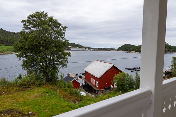 Ein traditionelles rotes Fischerhaus liegt idyllisch am Ufer der Küste von Hitra, Norwegen, umgeben von lebendigem Grün und ruhigem Wasser – ideal für einen entspannenden Angelurlaub in der Natur.