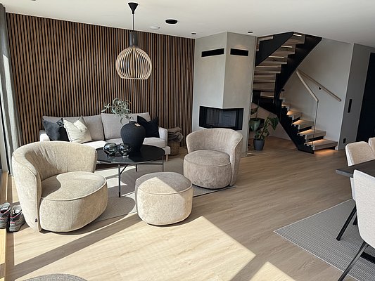 Ein modernes skandinavisches Wohnzimmer in Südwest-Norwegen mit eleganter Holzvertäfelung, bequemen Möbeln, rundem Couchtisch, Kamin und stilvoller Treppe. Perfekt für Erholung nach einem abenteuerlichen Angelurlaub in Norwegen.